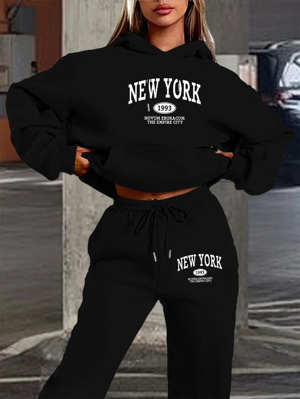 Person wearing a black 'New York' hoodie and sweatpants set with text on a blurred street background.