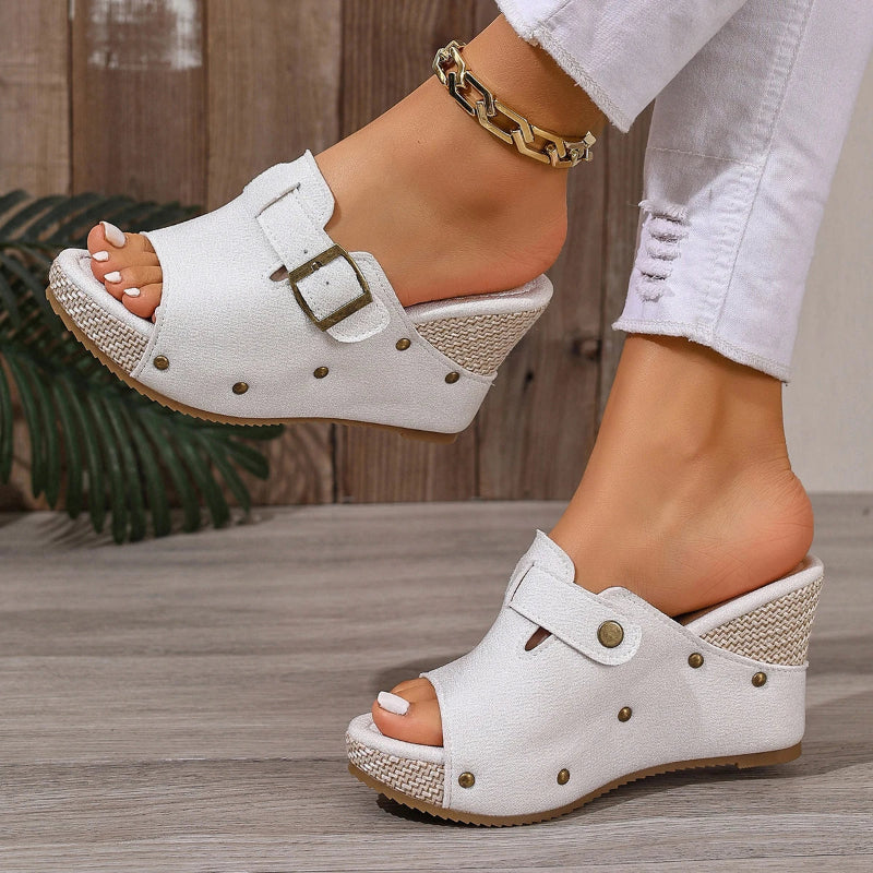 White clogs with brown soles worn by a person on a wooden floor.