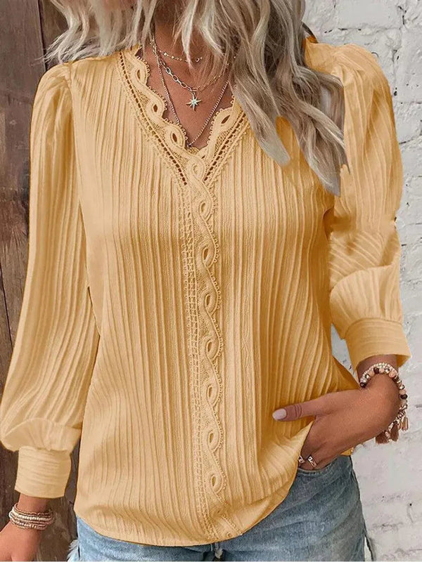 Woman wearing a yellow blouse with intricate details, standing against a wooden and white brick wall.