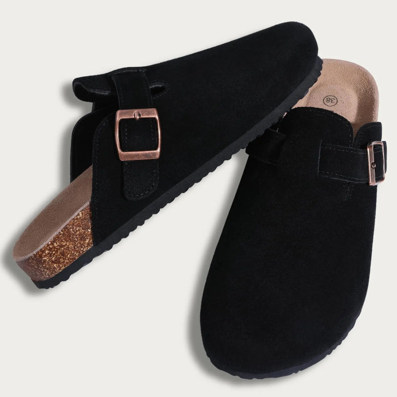 Black suede clogs with rose gold buckles on a light gray background