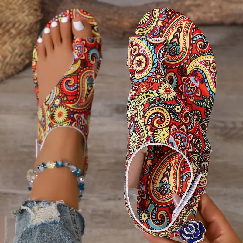 Colorful paisley-patterned sandals being worn and held by a person.