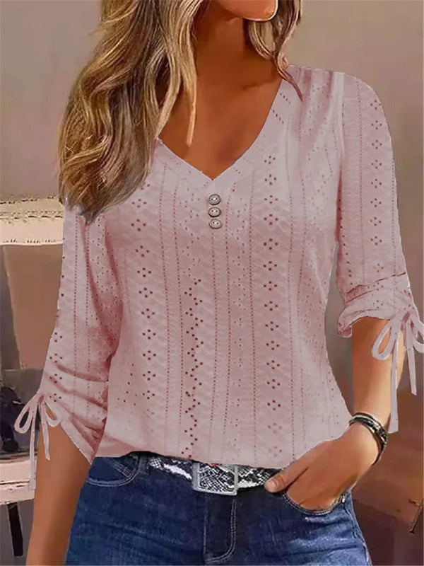 Woman wearing a light pink blouse with lace details and blue jeans indoors.