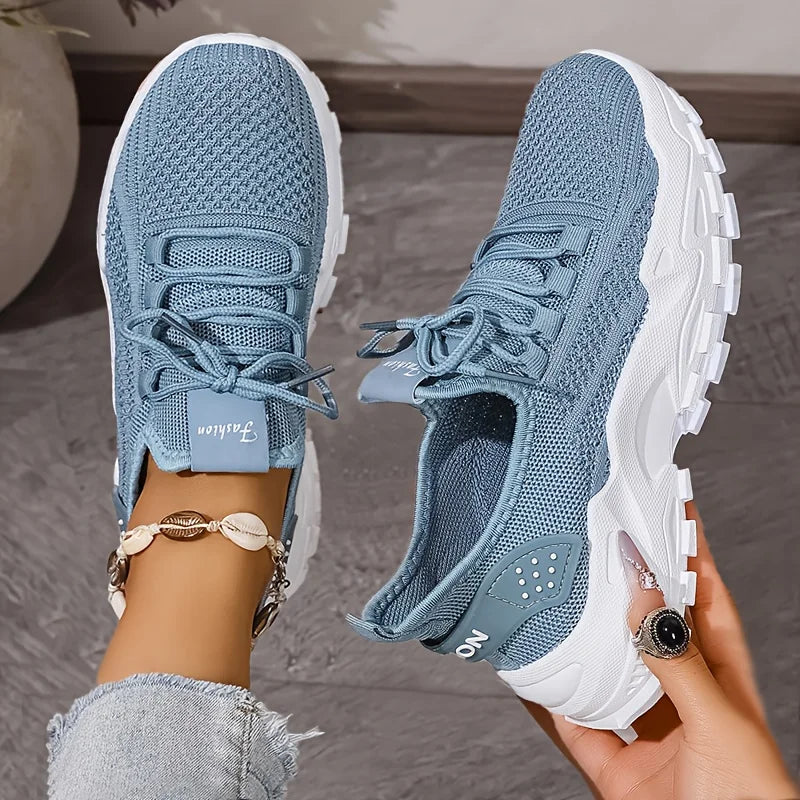 Blue athletic shoes with white soles held by a person against a neutral background