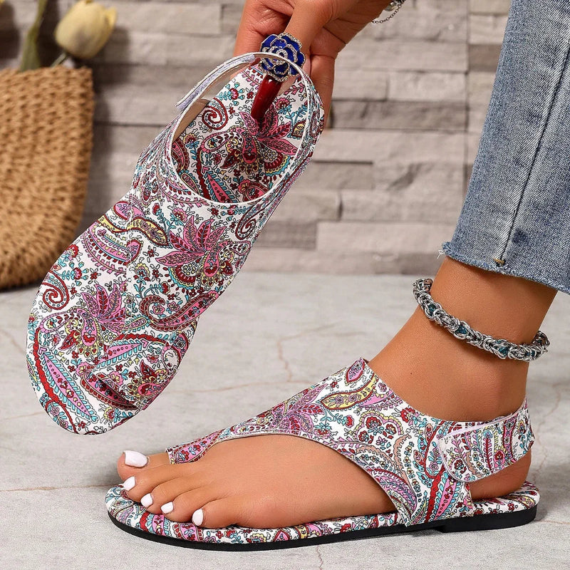 Multicolored paisley patterned sandals worn by a person on a wooden floor.