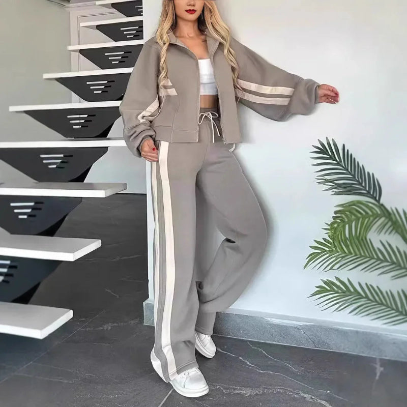 Woman in a gray tracksuit standing in front of a staircase with a plant in the background