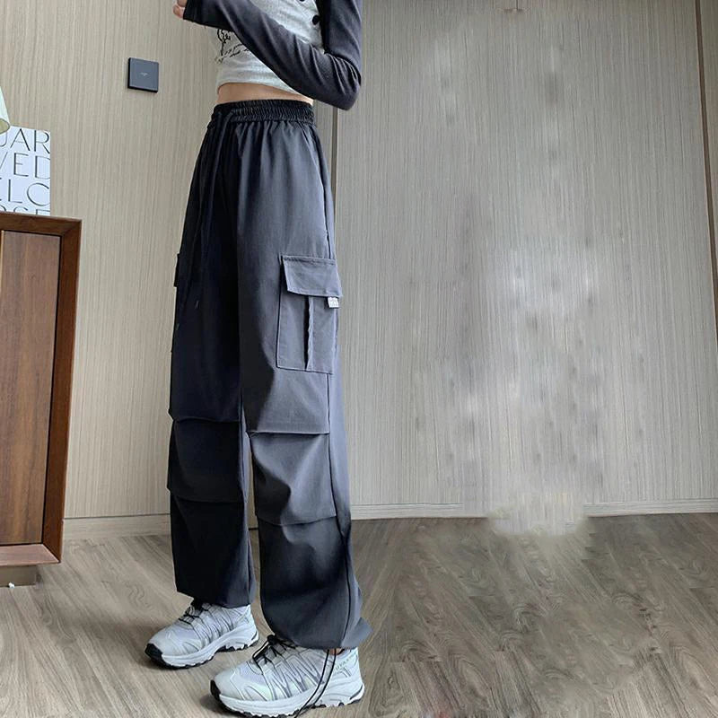 Person wearing dark gray cargo pants standing in a room with wooden flooring and a neutral wall.