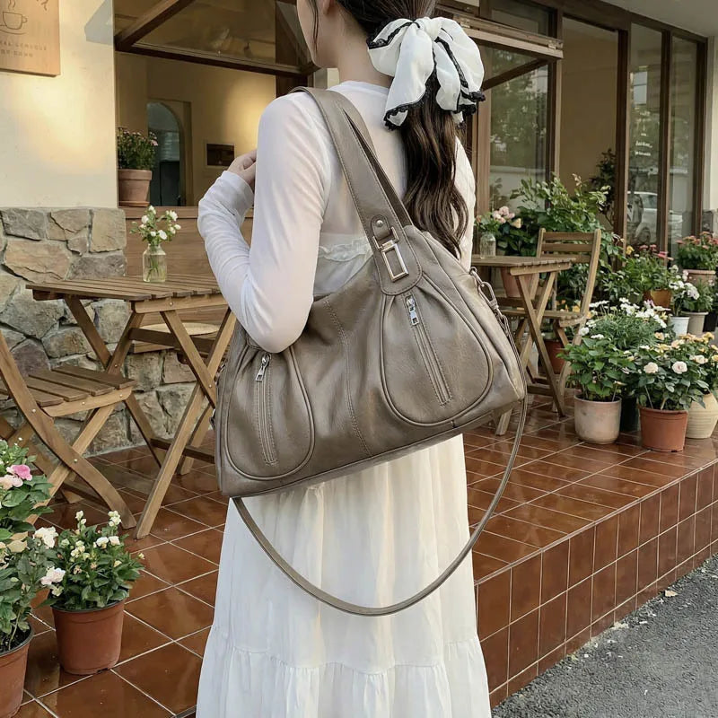 Woman holding a beige handbag in an outdoor setting with tables and plants.