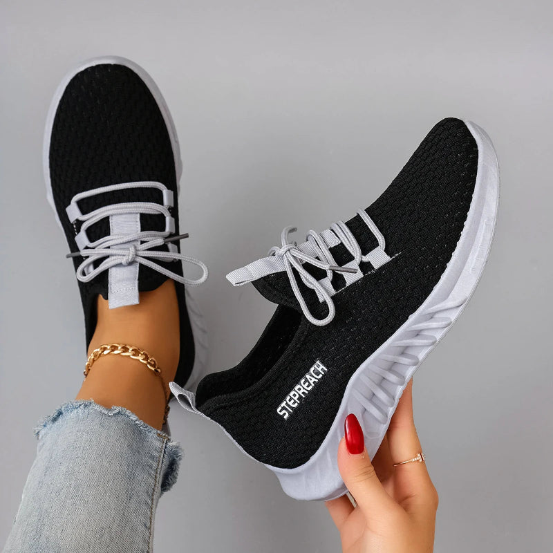 Black and white sneakers with 'Step Reach' branding held by a person against a gray background