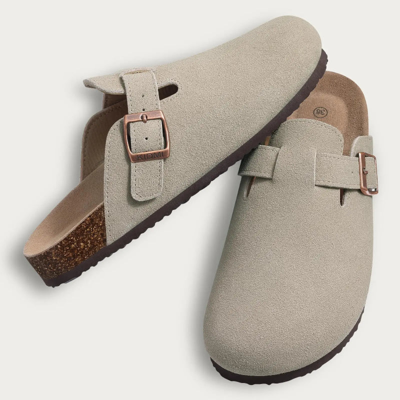 Pair of beige clogs with a buckle on a light gray background