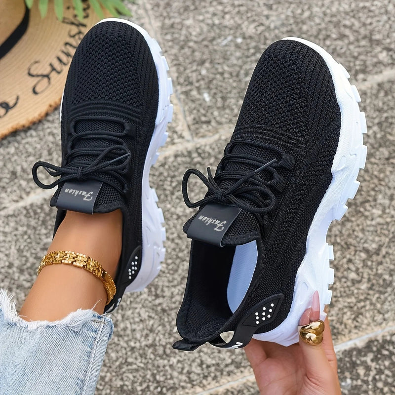 Black sneakers with white soles held by a person on a textured surface