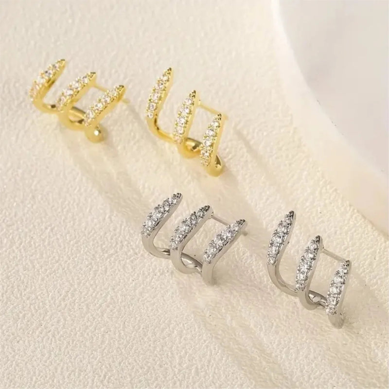 Gold and silver hoop earrings on a textured beige surface