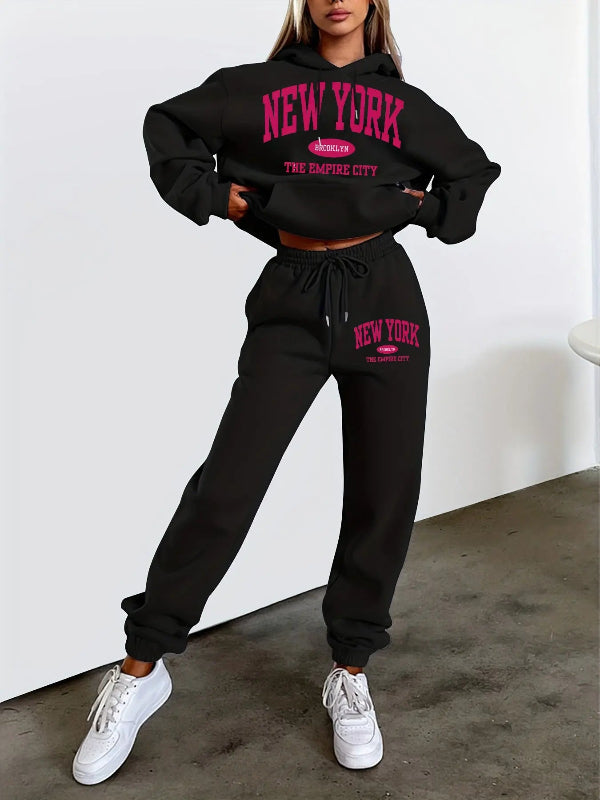Person wearing a black 'New York' hoodie and sweatpants set with white sneakers on a plain background