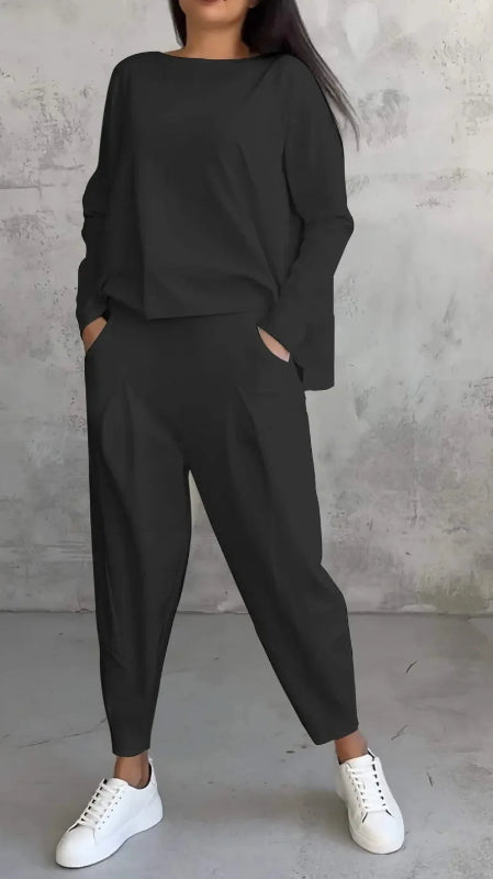 Person wearing a black outfit with white sneakers against a gray concrete wall.