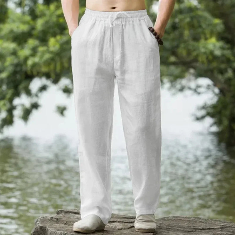 Person wearing light gray pants standing by a water body with greenery in the background