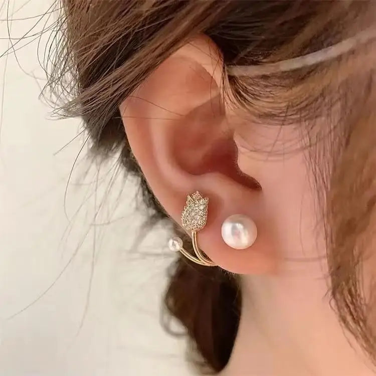 Close-up of an ear wearing a gold earring with a pearl and a diamond-studded design.