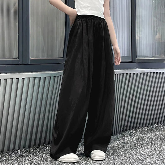 Person wearing black wide-leg pants and white shoes standing against a metallic wall.