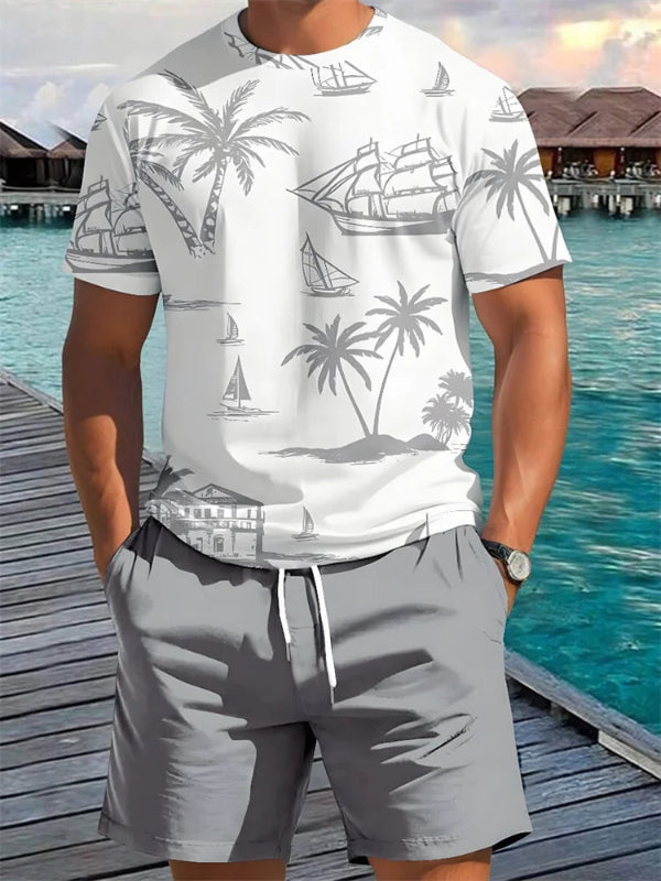 Person wearing a white t-shirt with gray palm tree and ship design and gray shorts by a waterfront.