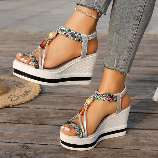 White wedge sandals with colorful embellishments on a wooden floor.