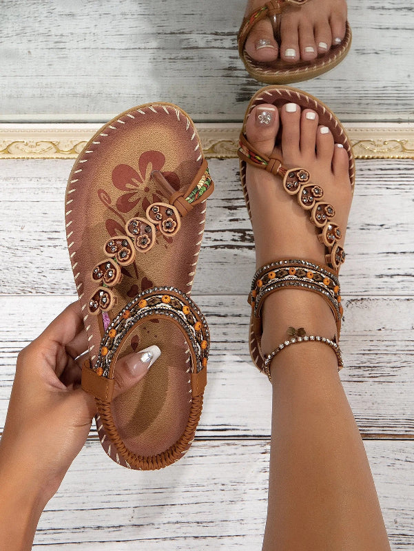 Brown embellished sandals being worn on a wooden floor