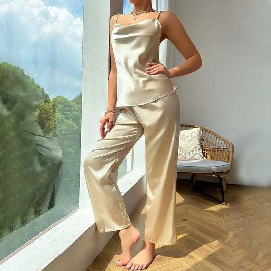 Woman in beige satin pajama set standing by a window with a view of greenery.
