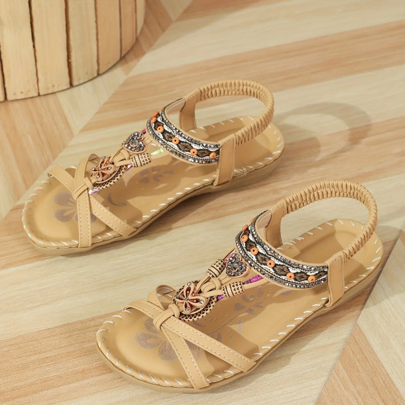 Pair of beige sandals with decorative straps on a wooden surface