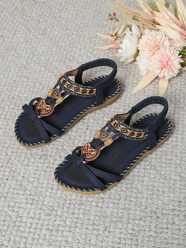 Navy sandals with decorative straps on a textured surface with flowers.