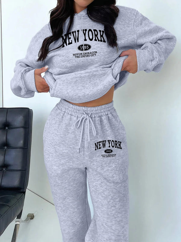Person wearing a gray 'New York' sweatshirt and pants set against a white background.