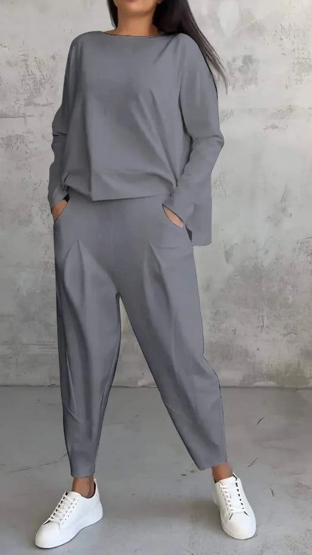 Person wearing a gray outfit with white sneakers against a concrete wall.