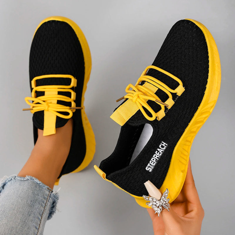 Black and yellow sneakers with 'SKECHERS' branding held by a person wearing a silver ring.