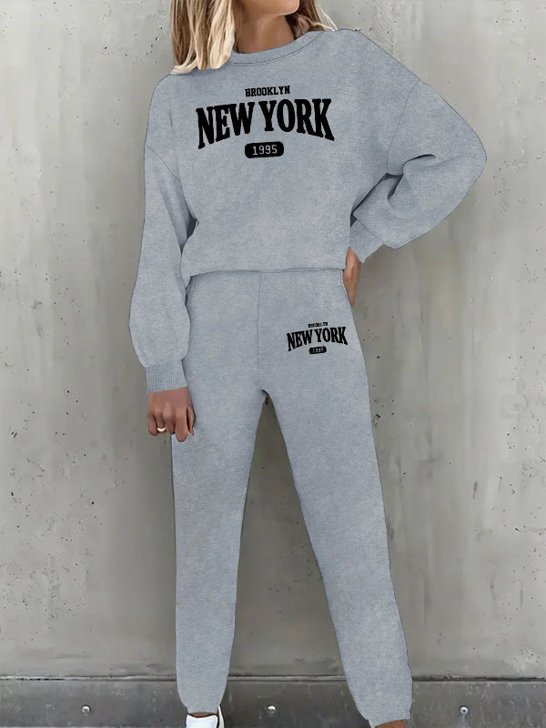 Person wearing a gray 'New York' sweatshirt and pants against a concrete wall.