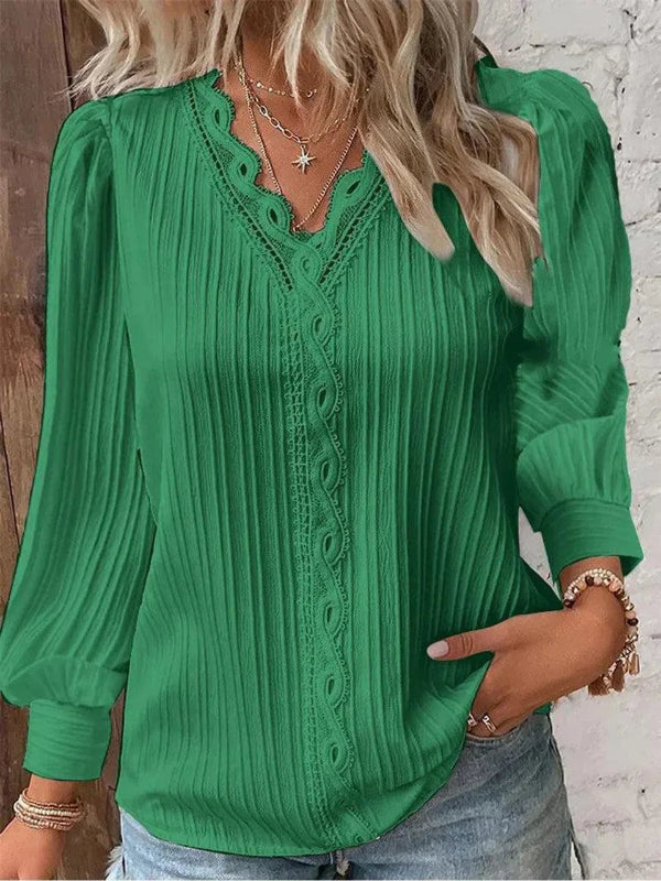 Green blouse with lace details worn by a person, against a wooden and white brick wall background.