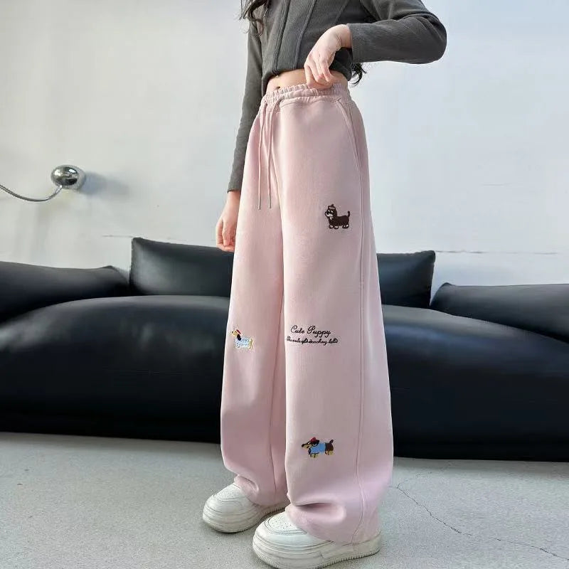 Person wearing pink sweatpants with embroidery designs in a minimal indoor setting.