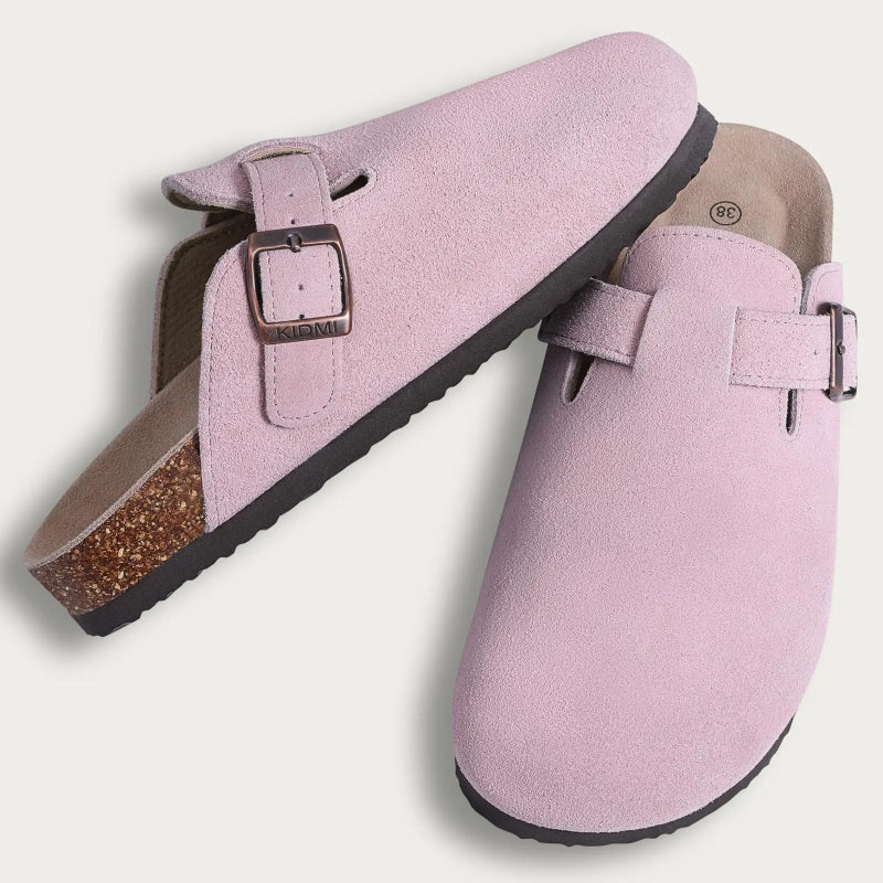 Pair of pink suede clogs with a buckle on a light gray background