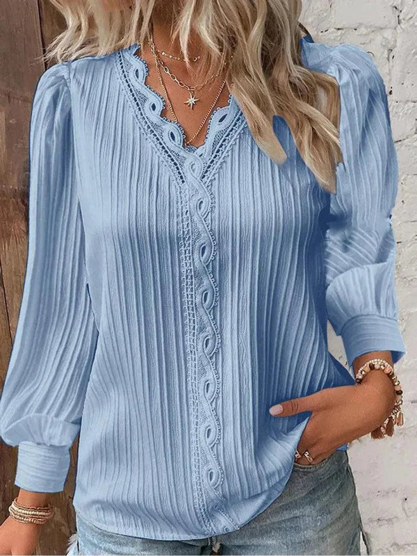 Woman wearing a light blue blouse with lace details and long sleeves.