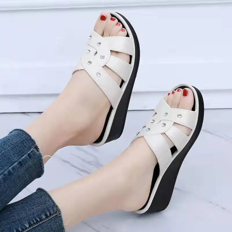 White sandals with black soles worn by a person on a light wooden floor.