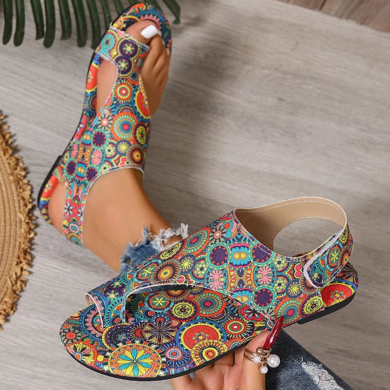 Colorful floral-patterned sandals being worn on a wooden floor.