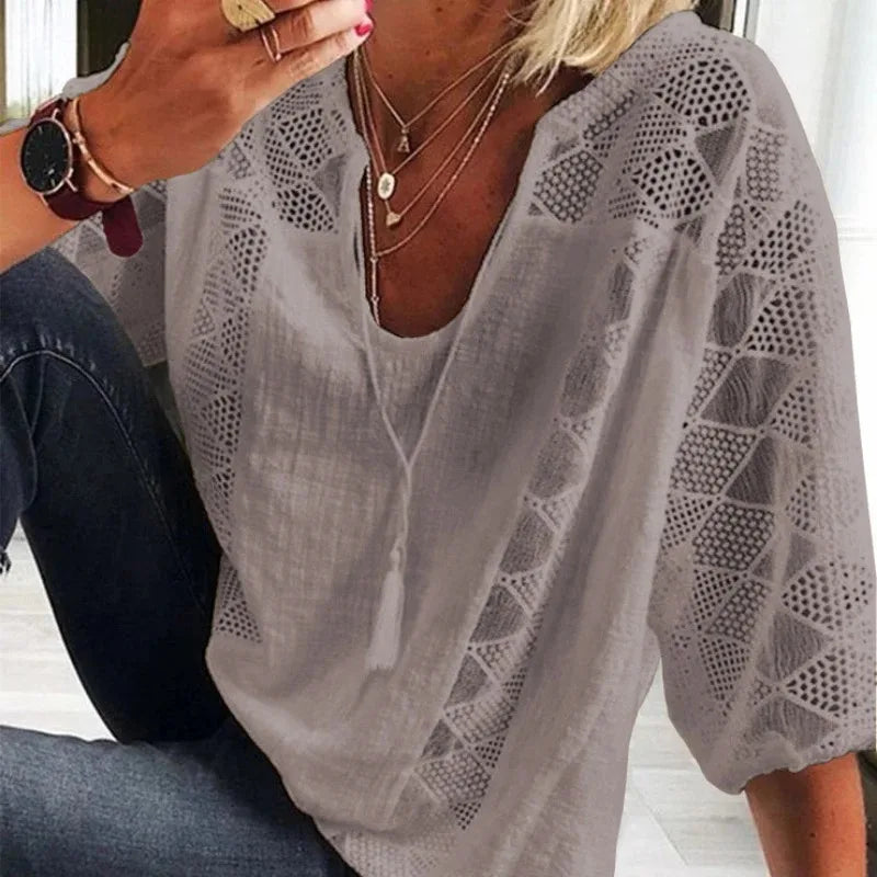 Person wearing a light gray blouse with geometric patterns on a blurred indoor background