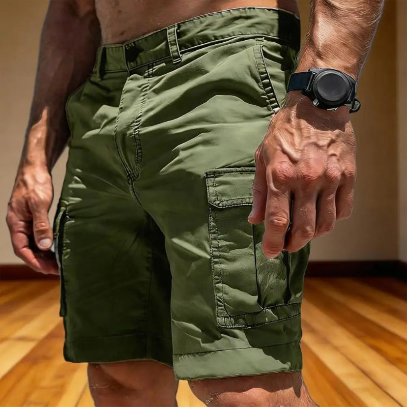 Person wearing green cargo shorts and a black watch on a wooden floor.