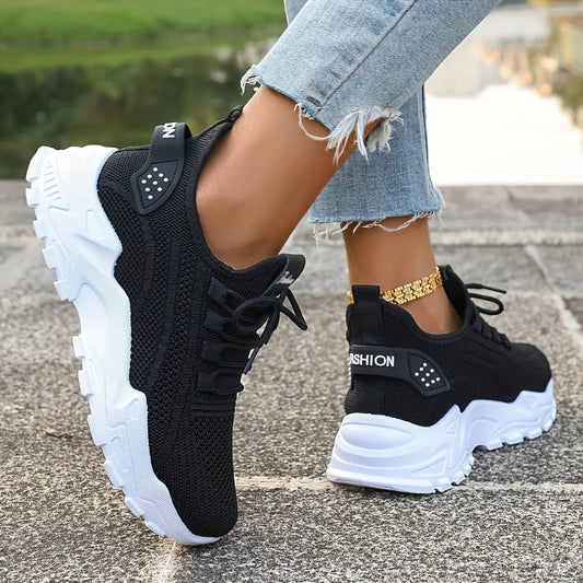Black sneakers with white soles worn by a person on a blurred outdoor background