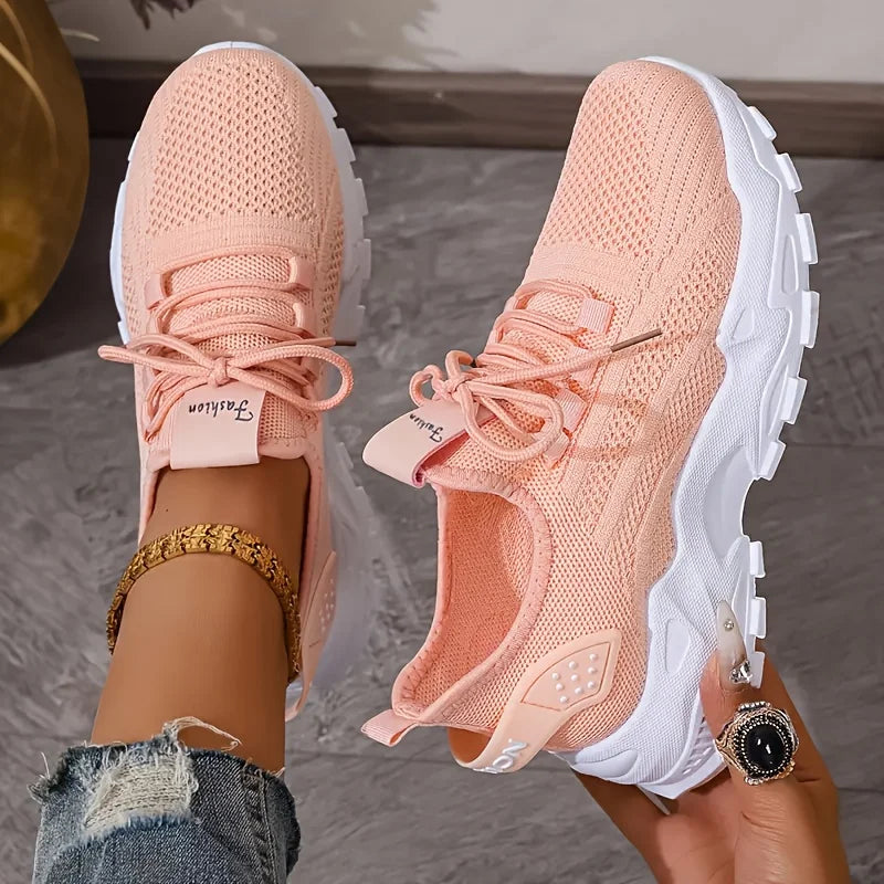 Pair of pink sneakers with white soles worn by a person on a neutral background