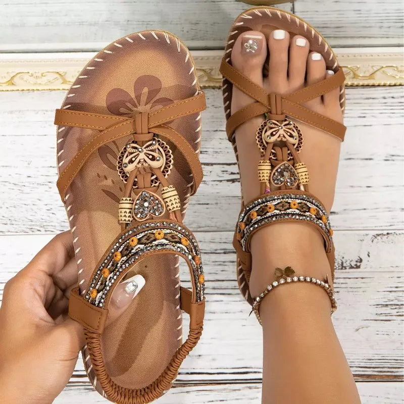 Brown sandals with decorative straps and embellishments on a wooden floor.