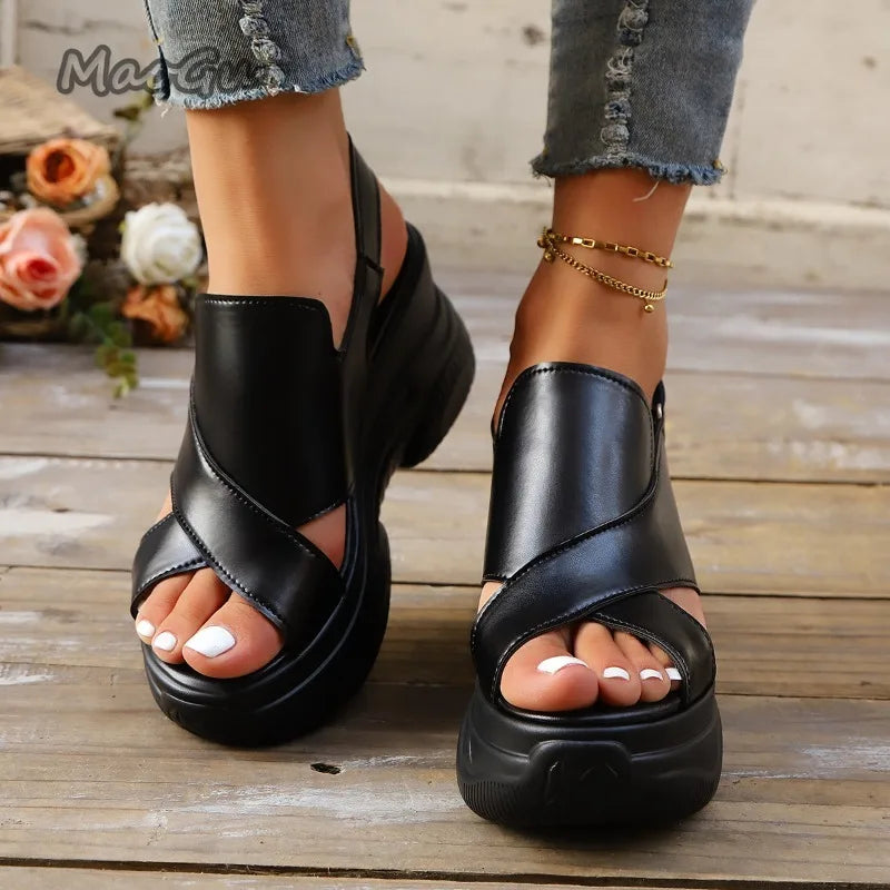 Black sandals worn on feet with denim jeans on a wooden floor.