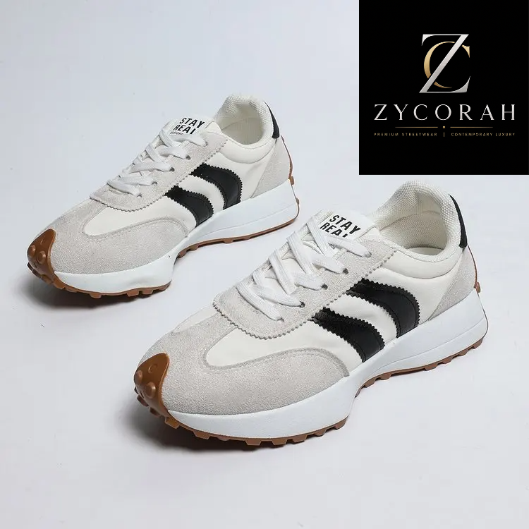 A pair of low-top sneakers shown on a clean light gray studio background, with a black brand panel in the top-right corner. The shoes have off-white suede and mesh panels, black side stripes, white laces, a white midsole, and brown rubber toe caps and outsoles.