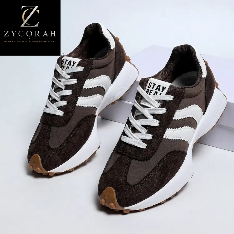 A pair of low-top sneakers in dark brown and white, featuring white laces, white side stripes, and a chunky white sole with a gum outsole. The brand logo 'ZYCORAH' is visible in the top-left corner.