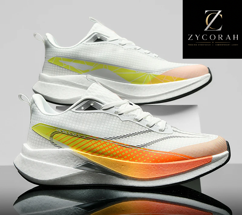 A pair of white athletic sneakers with a vibrant yellow-to-orange gradient side stripe, displayed on a reflective gray surface with a ZYCORAH brand logo in the top right corner.