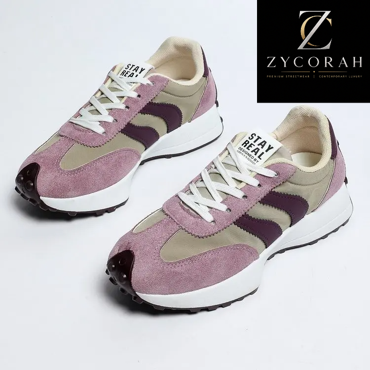 A pair of low-top sneakers in dusty pink suede and beige mesh with dark purple side stripes, white laces, and white midsoles. The shoes are displayed on a clean white background with a black brand logo overlay in the top right corner reading 'ZYCORAH'.