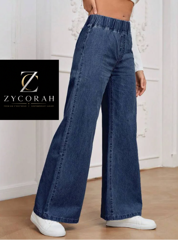 A model wearing high-waisted, wide-leg blue denim jeans with an elastic waistband, styled with a white crop top and white sneakers. A brand logo overlay for 'ZYCORAH' is visible on the left side.