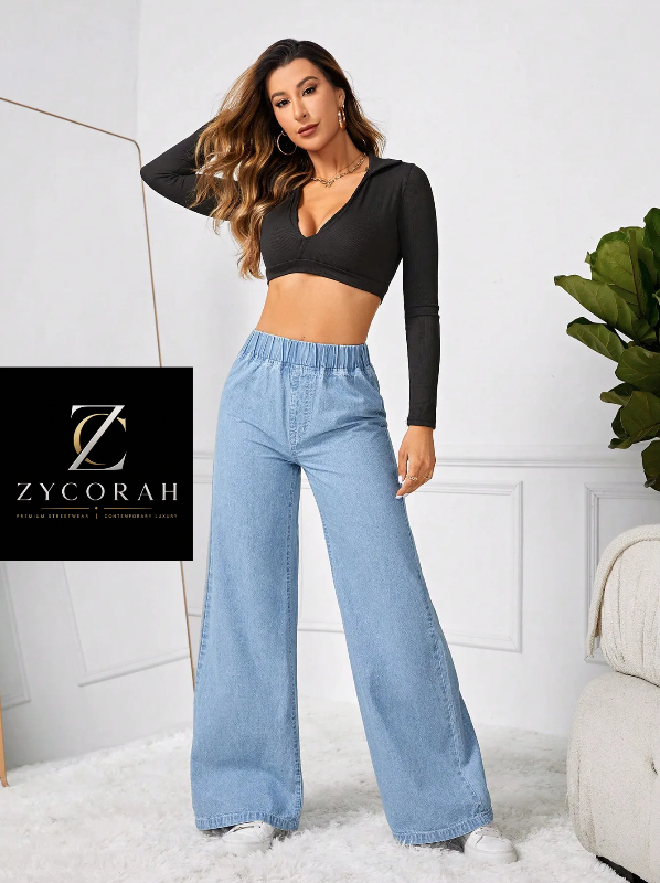 A woman models a black long-sleeve wrap-style crop top and light blue wide-leg jeans, standing in a bright indoor room with a white wall, rug, and plant. A ZYCORAH logo card is overlaid on the left side.
