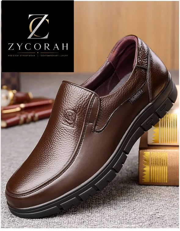 A brown pebbled leather slip-on shoe with a black sole, displayed on a textured gray surface with decorative books in the background. A black brand panel at the top reads 'ZYCORAH' and the left side has Chinese text.