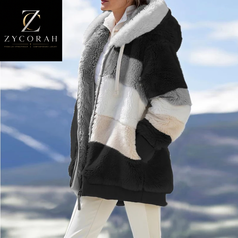 A woman wearing a chunky color-block teddy coat with a white faux-fur collar and hood, set against a blurred mountain background. A black brand overlay for 'Zycorah' is in the top-left corner.